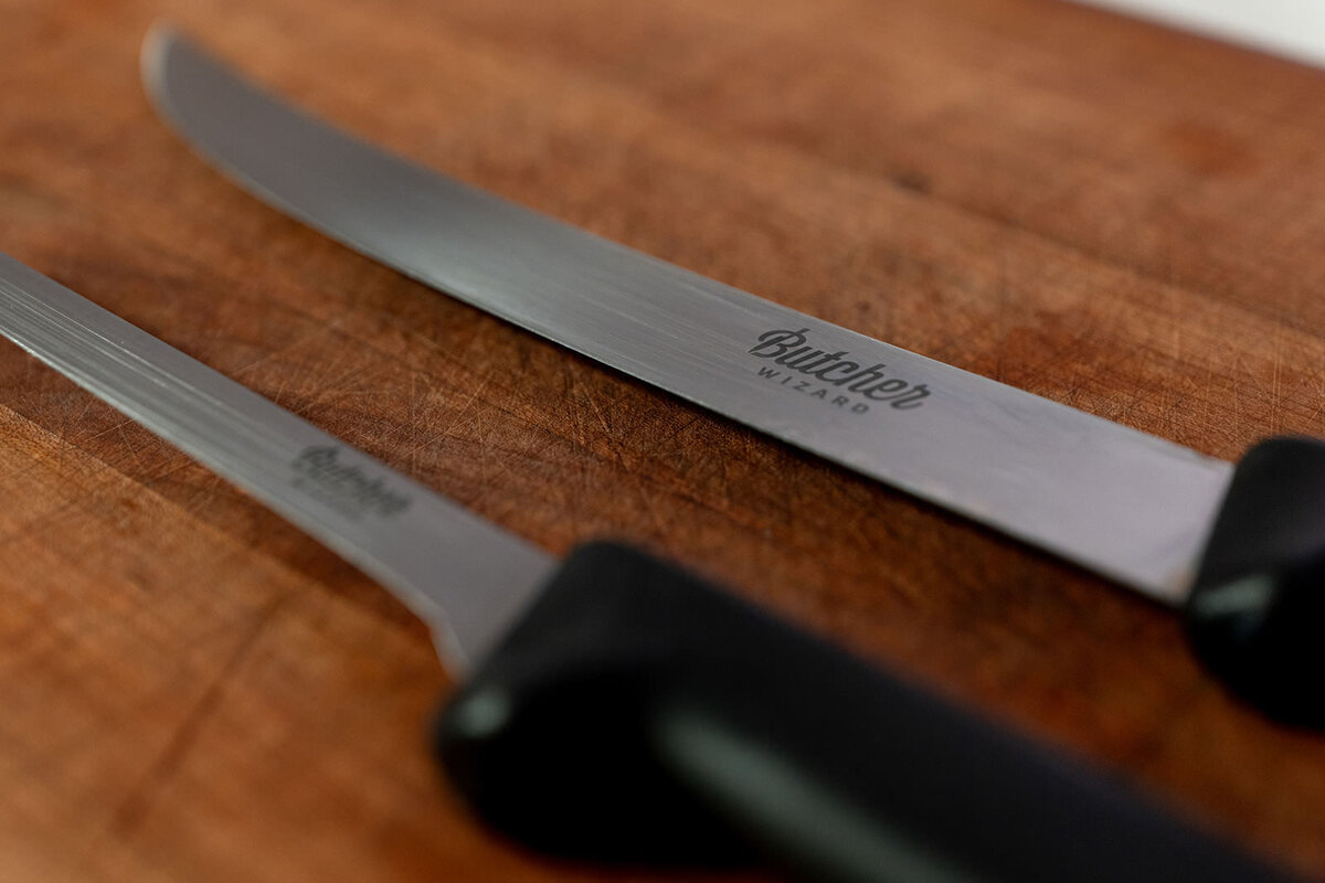 Two thin knives laying next to each other on a cutting board 