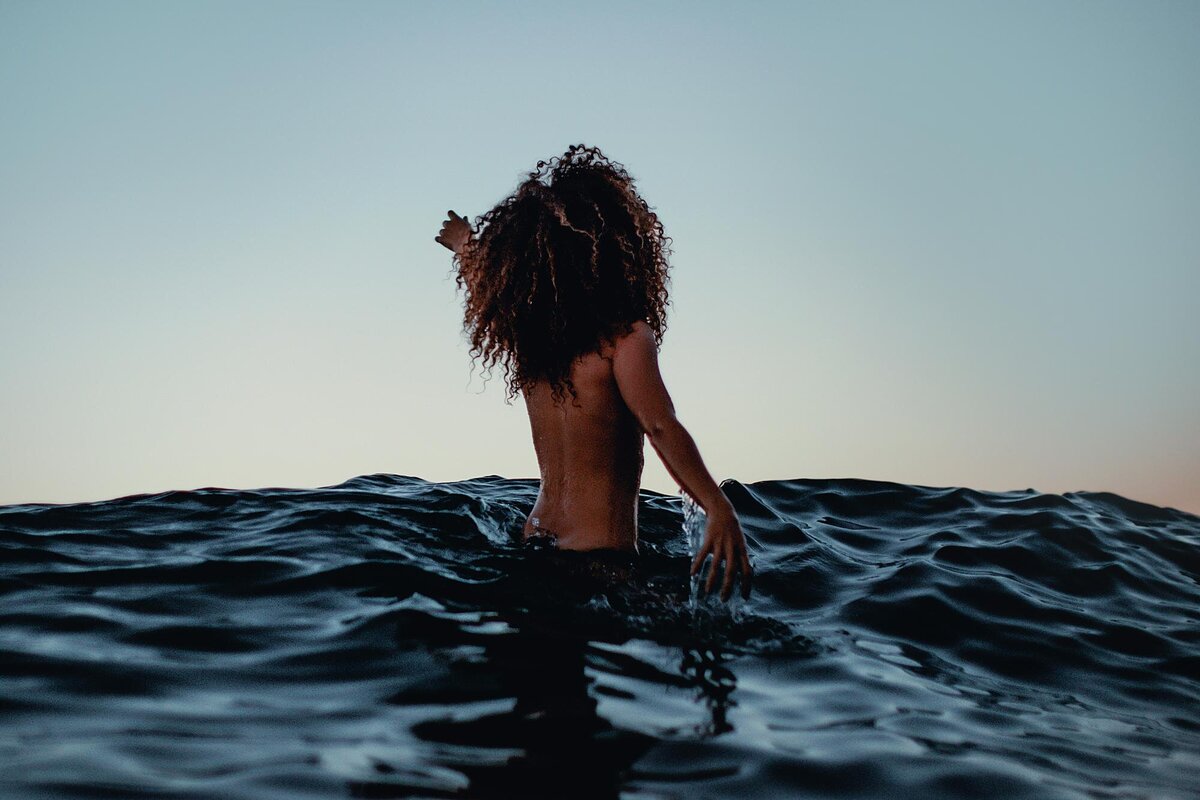 Sunset boudoir portrait of a woman walking into the ocean under the moonlight