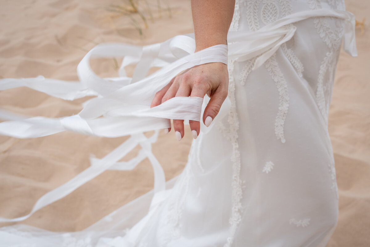 Closeup of bride's Claire Pettibone lace with ribbons gown at Kelso Dunes at sunrise