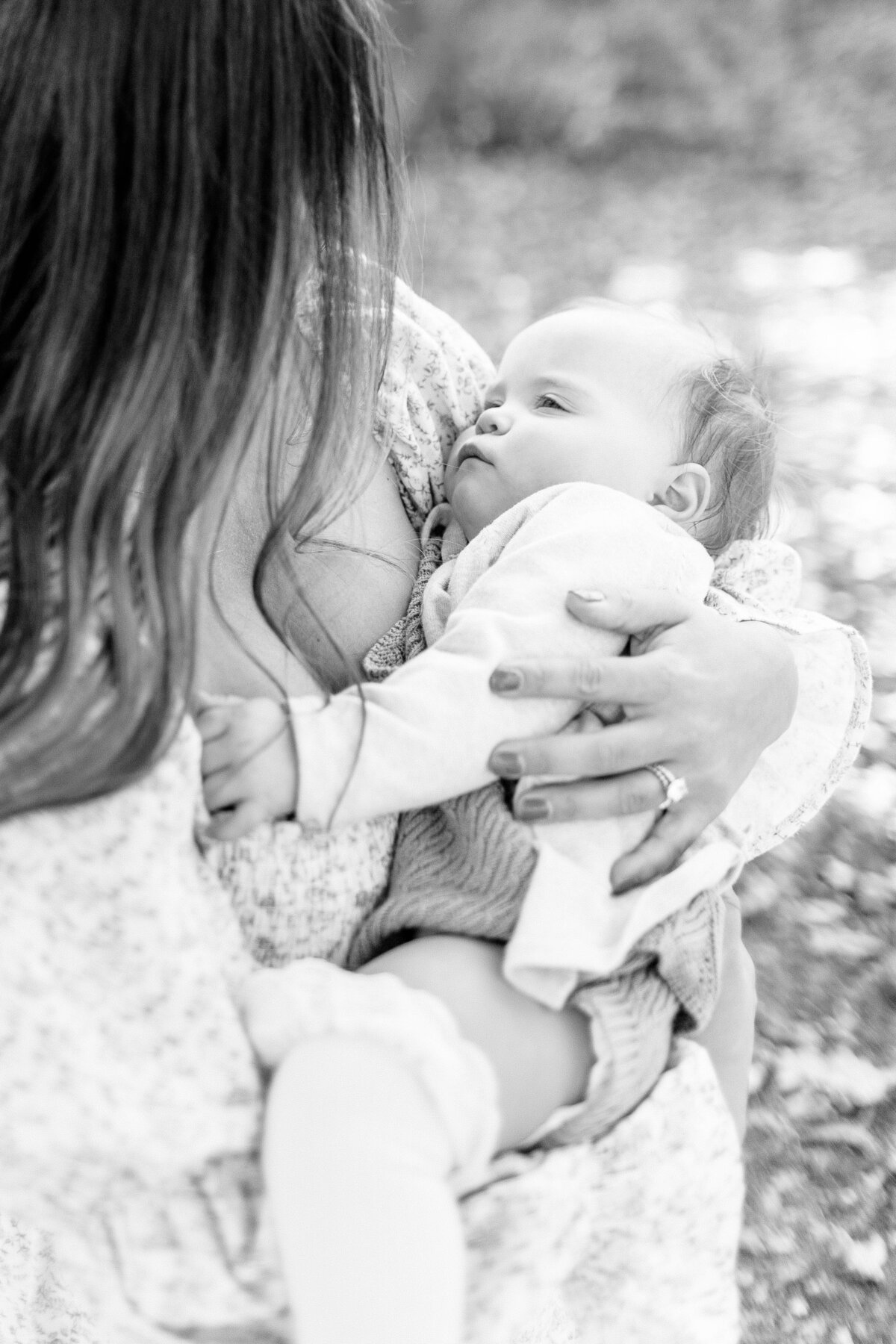 Black and white image of mother cradling her one year old daughter outdoors during a quiet moment at a Kansas City milestone session.
