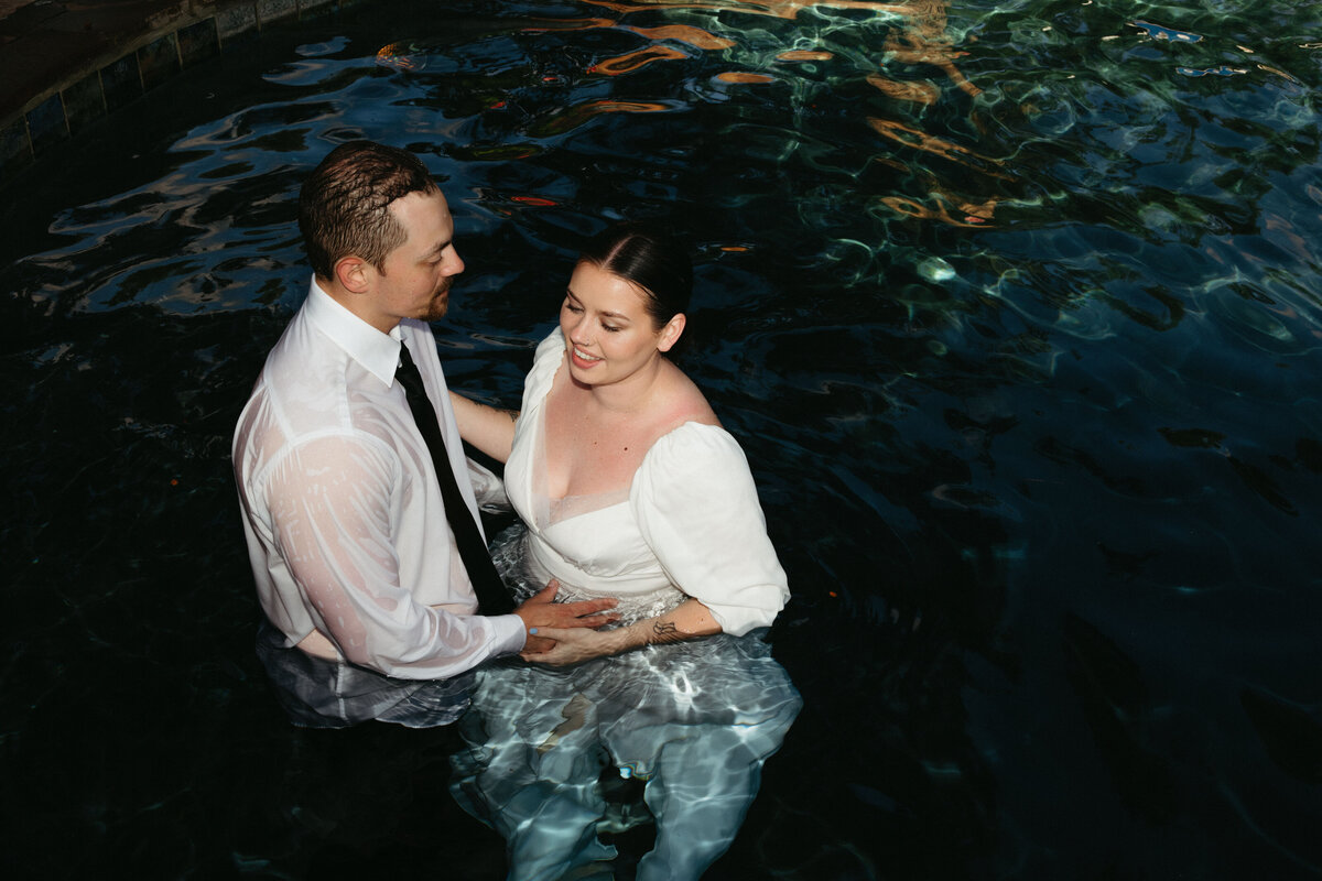 Bride and Groom in pool in their wedding clothes holding hands