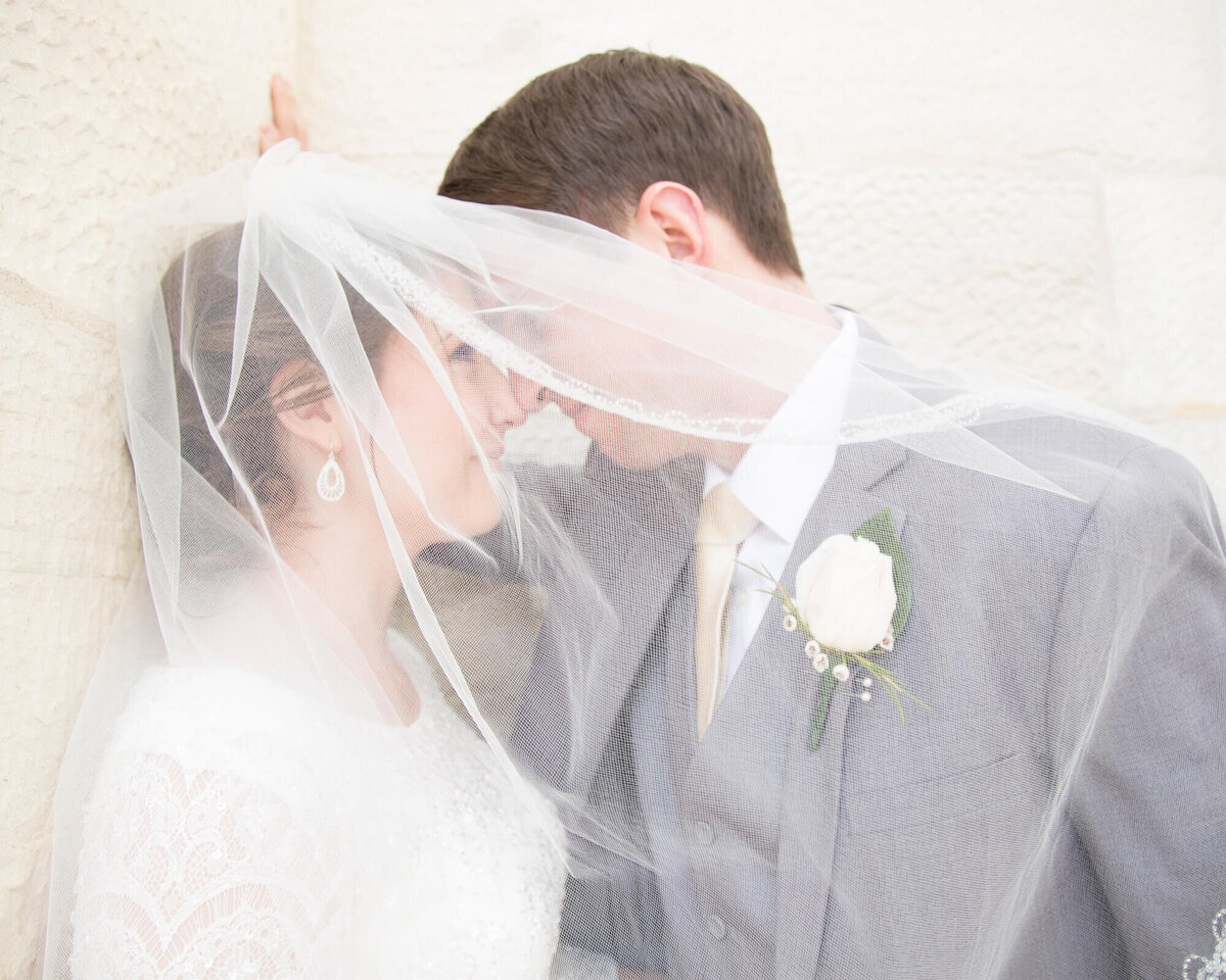 bride against a stone wall smiling at groom under her veil