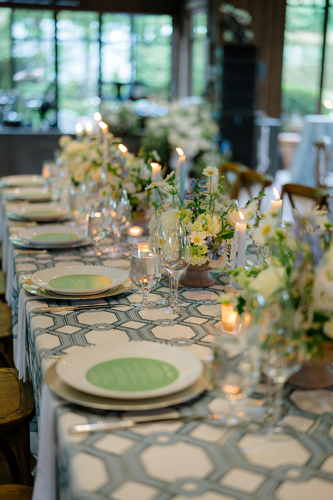 Long reception table with white and soft blue florals, tapered candles, and layered place settings.