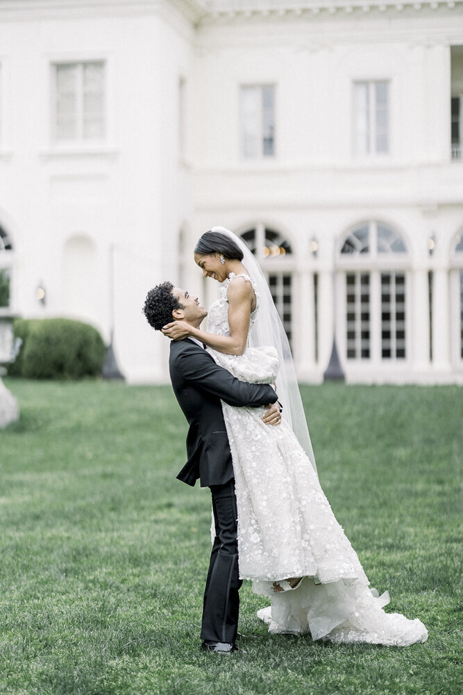 a groom lifting up his bride on the lawn of a mansion
