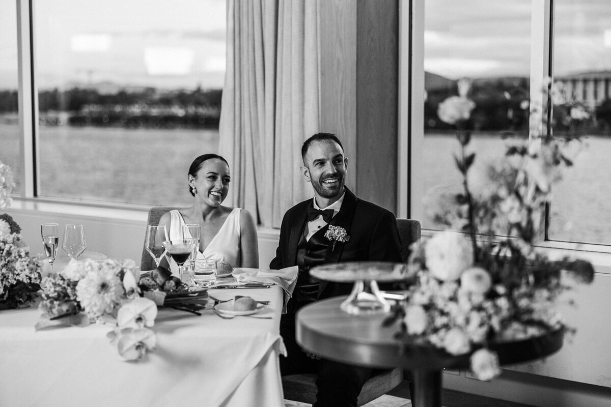 Bride and groom smile during family speeches at their wedding