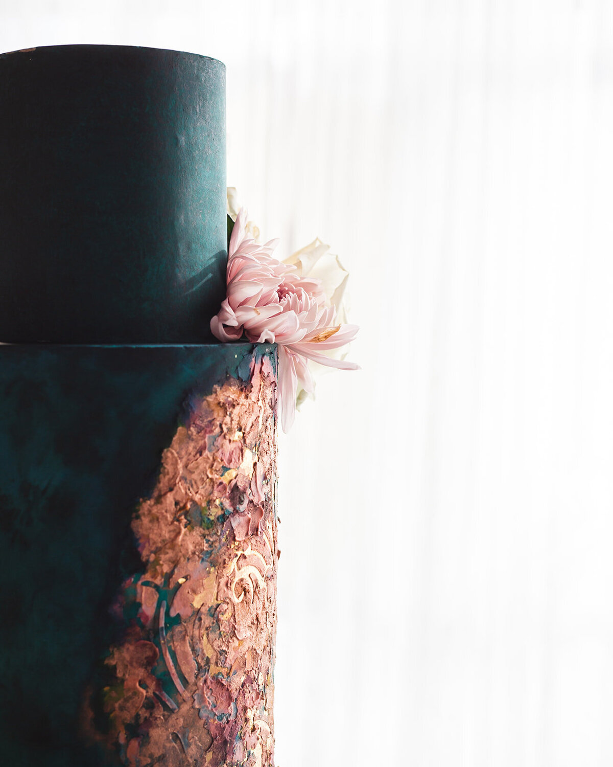 close up of a teal wedding cake with a pink flower sitting in between teirs