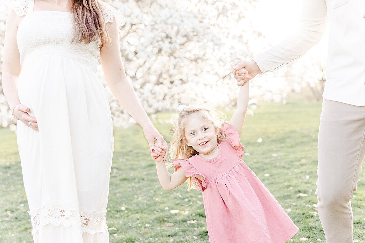 parents hold daughters hands during spring maternity photo session in Wellesley Massachusetts with Sara Sniderman Photography