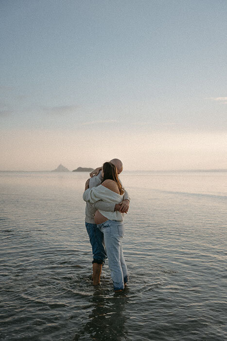 Couple enlacé les pieds dans l'eau pendant un shooting photo grossesse à la plage.
