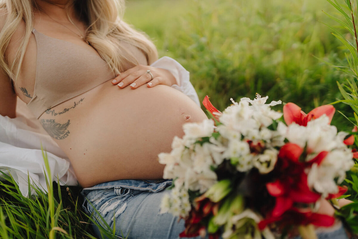 woman laying on grass holding baby bump at  maternity session in Finger Lakes, New York