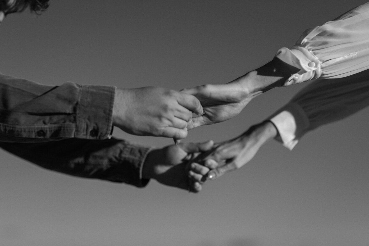 close up of the hands of partners holding hands, extended out with the sky in the background