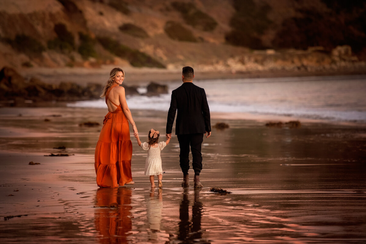 mom in orange golden summer beach dress walking with family and looking back.