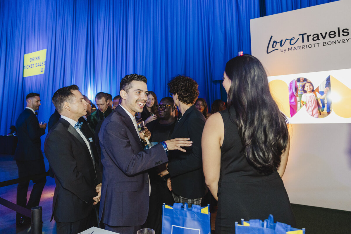 People are deep in conversation while blue bags stand on a table in the foreground.
