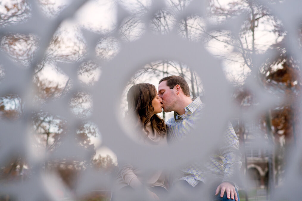 A couple kisses in front of a circular metal frame.