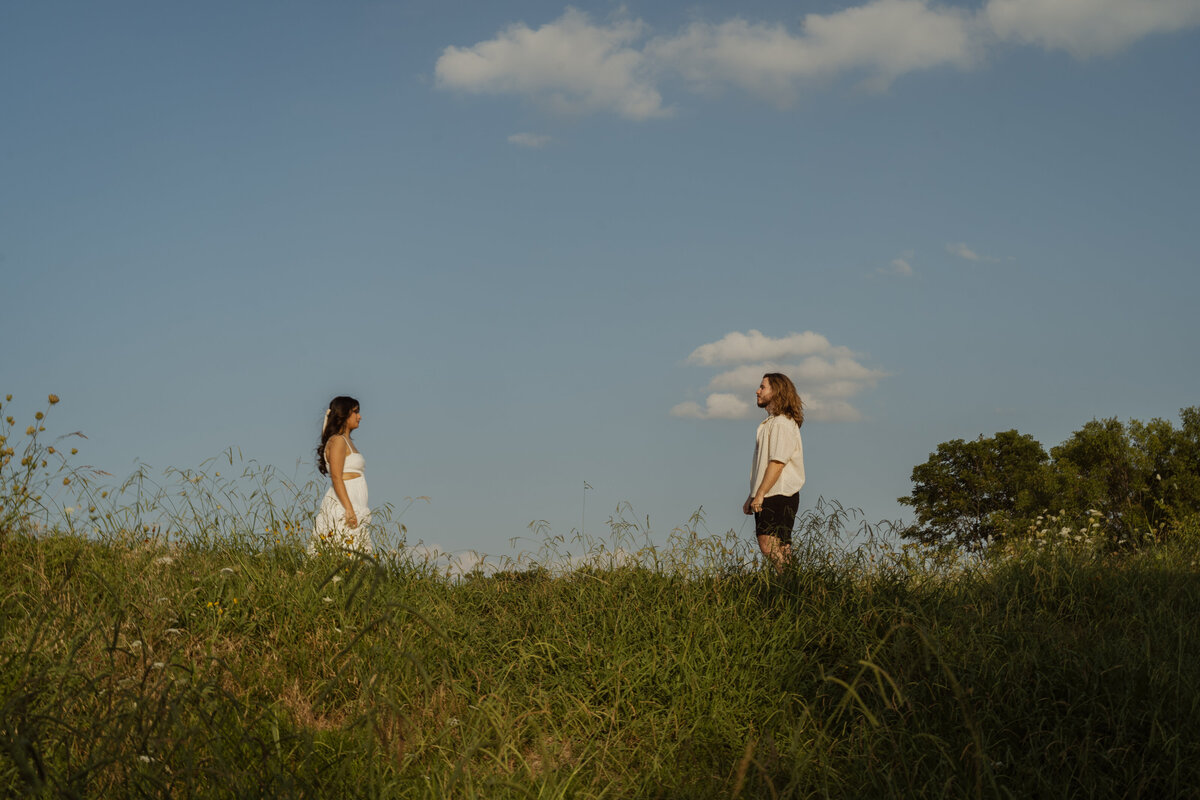 A serene, outdoor portrait of a couple standing apart on a grassy hill under a clear blue sky in the park near White Rock Lake, Dallas. This engagement session captures the peaceful connection and natural beauty of the location, perfect for showcasing love in a picturesque Dallas setting.