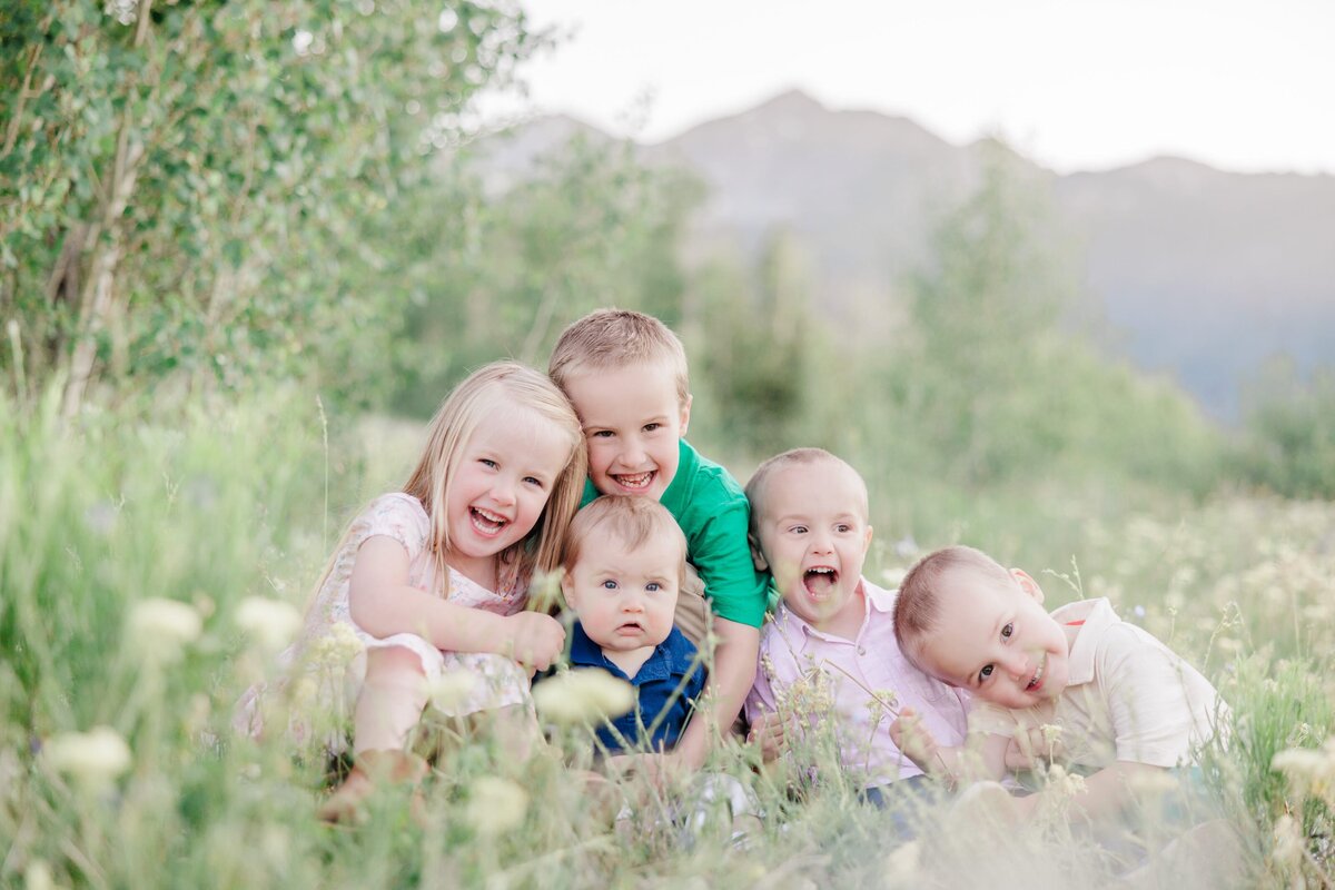 A group of 5 toddler siblings laughing while sitting and hugging in a mountain meadow captured by their Breckenridge Family Photographer