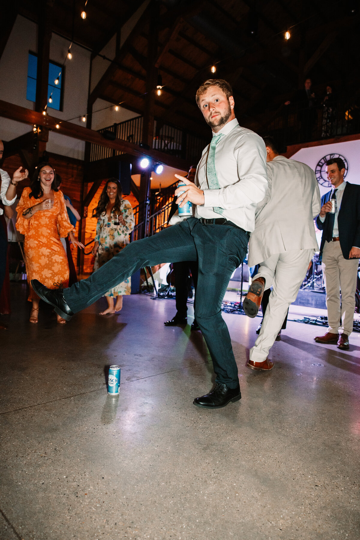 A man dances with a beer can with a leg up with the reception guests