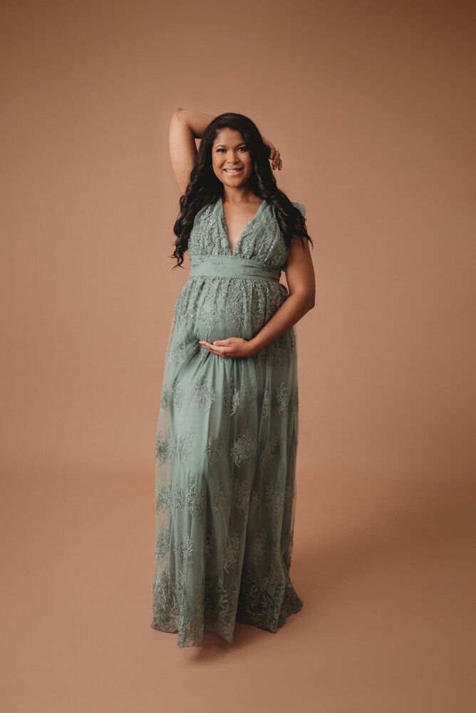 Maternity session with Atlanta, Georgia maternity photographer pregnant woman holding baby bump wearing siege green lace dress on tan backdrop