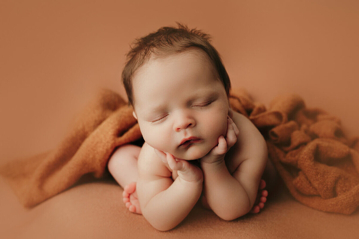 baby boy sleeping in froggy pose brown backdrop
