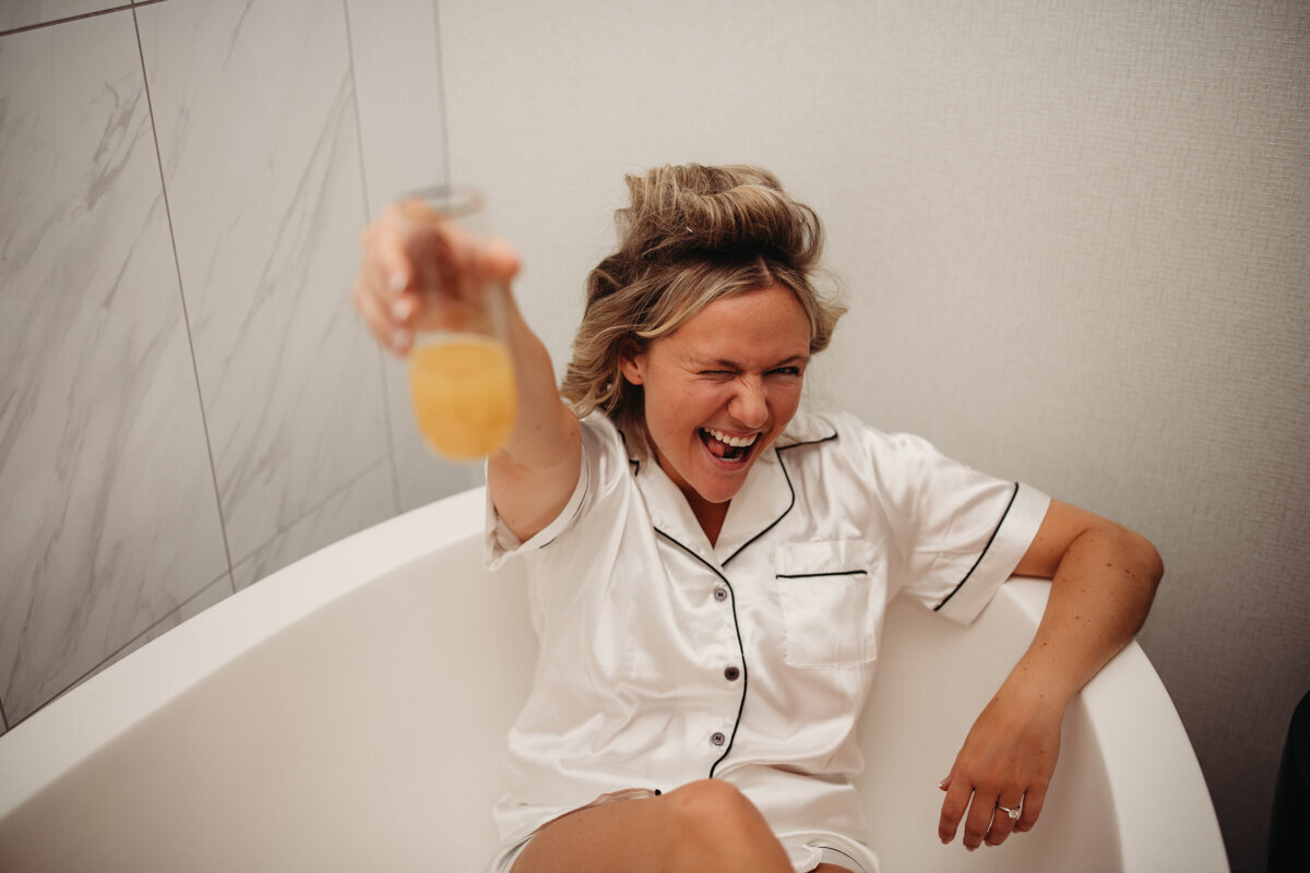 Bride toasts to camera while sitting in tub, non-traditional photographer at Cleveland HIlton