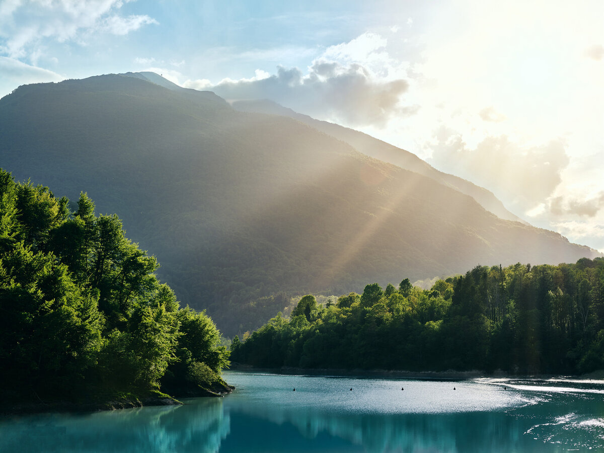 Sonnenlicht durchflutet die bewaldeten Hügel am Lago di Vernice – eine stimmungsvolle Gegenlichtaufnahme vom Spezialisten für Alpenlandschaften, Fotograf Atelier Schulte. Professionelle Landschaftsfotografie mit Fokus auf besondere Lichtstimmungen in Italien und Österreich.