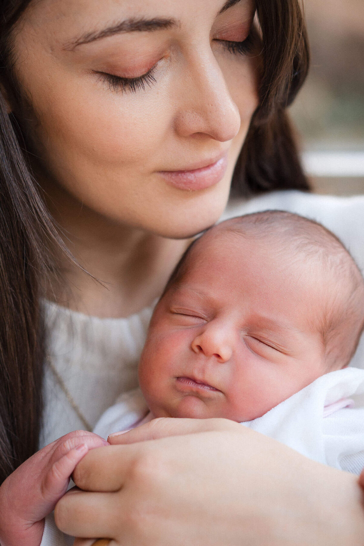 Mother holding her sleeping newborn close to her chest, both calm and still.