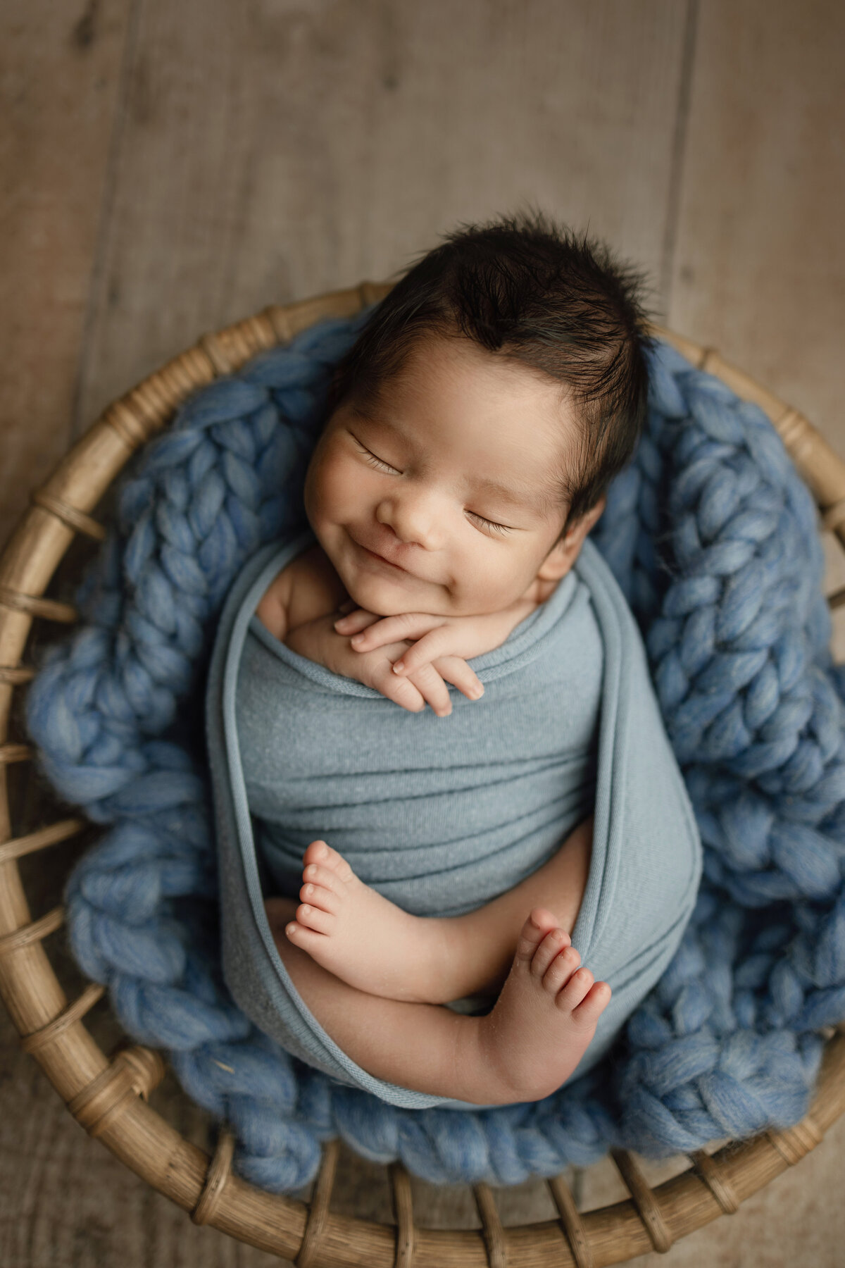 Newborn boy laying in a bowl wrapped in blue for his photo session