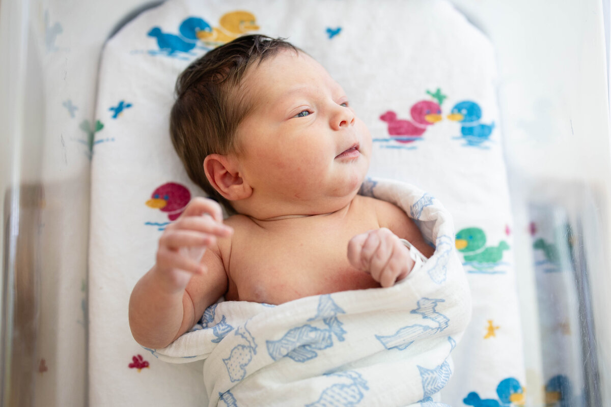 Newborn baby laying on duck blankets in bassinet