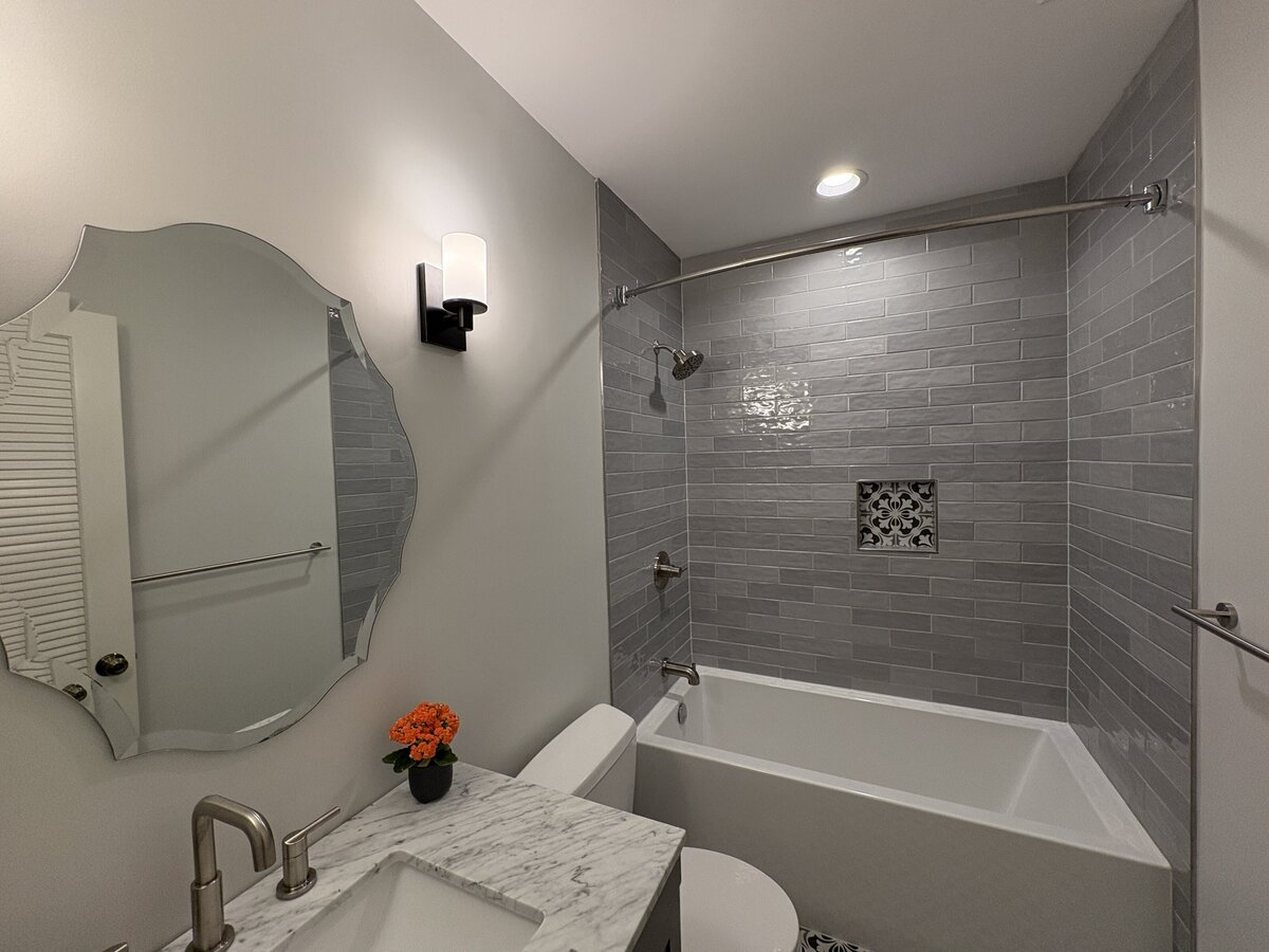 A remodeled bathroom featuring gray wall tile, patterned floor tile, a modern vanity, and a white tub-shower combination.