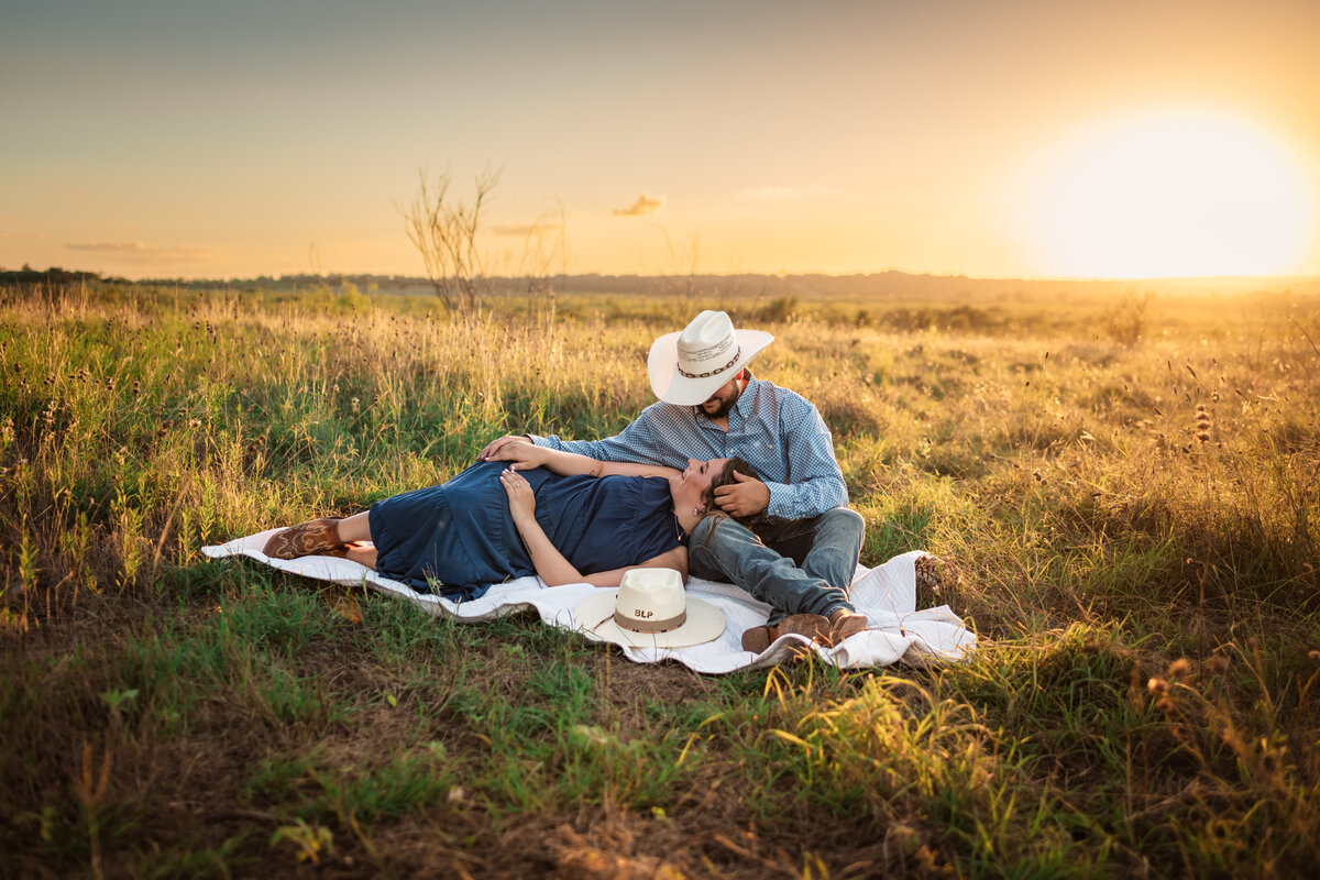 Engaged couple sitting on blanket in open field during sunset engagement session at Harper Hills in New Braunfels, Texas."