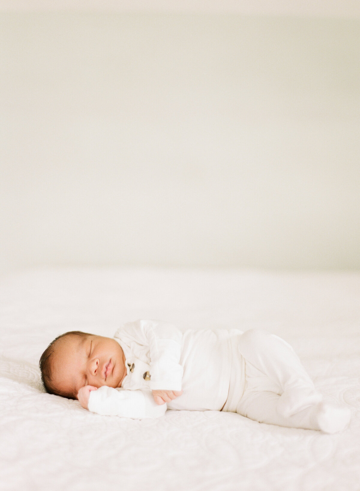 Newborn baby sleeps on a white blanket. Image by Raleigh newborn photographer A.J. Dunlap Photography.