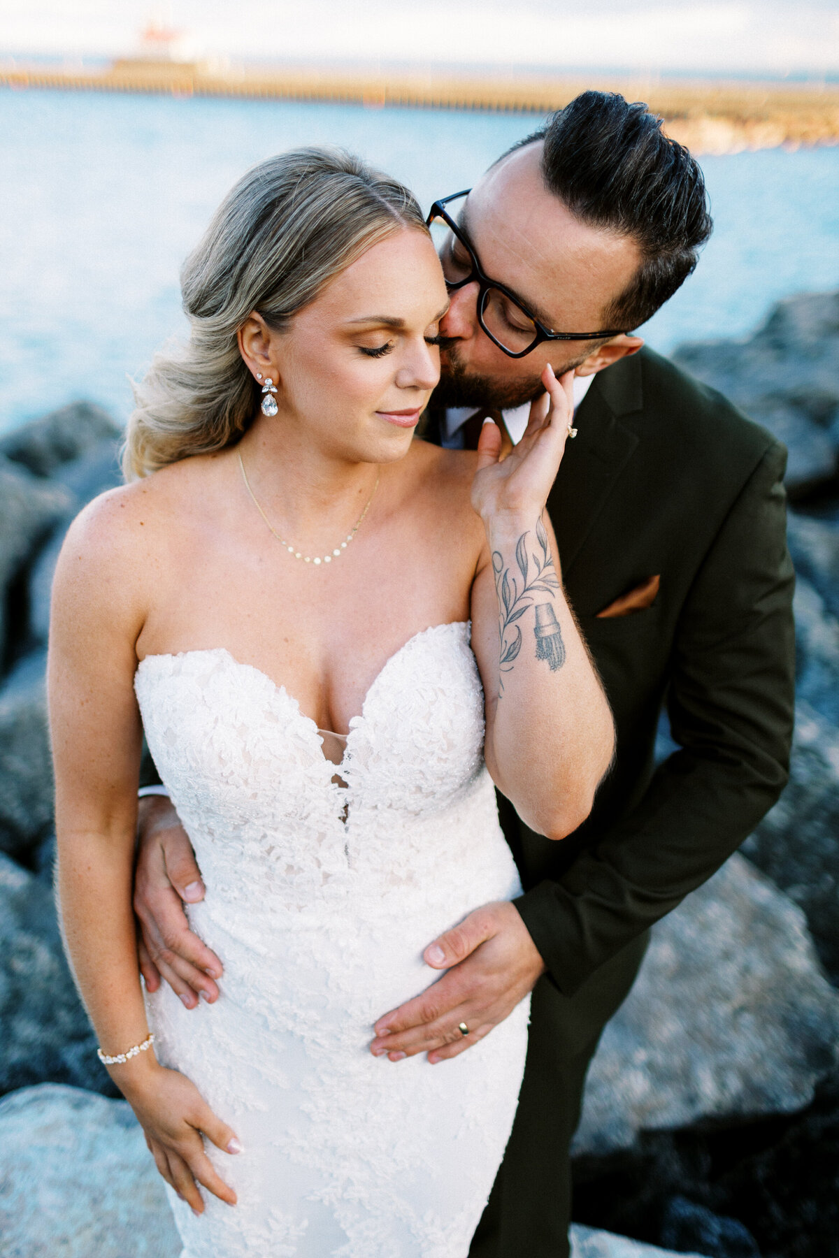 groom kissing his bride and holding her close with lake superior on the background