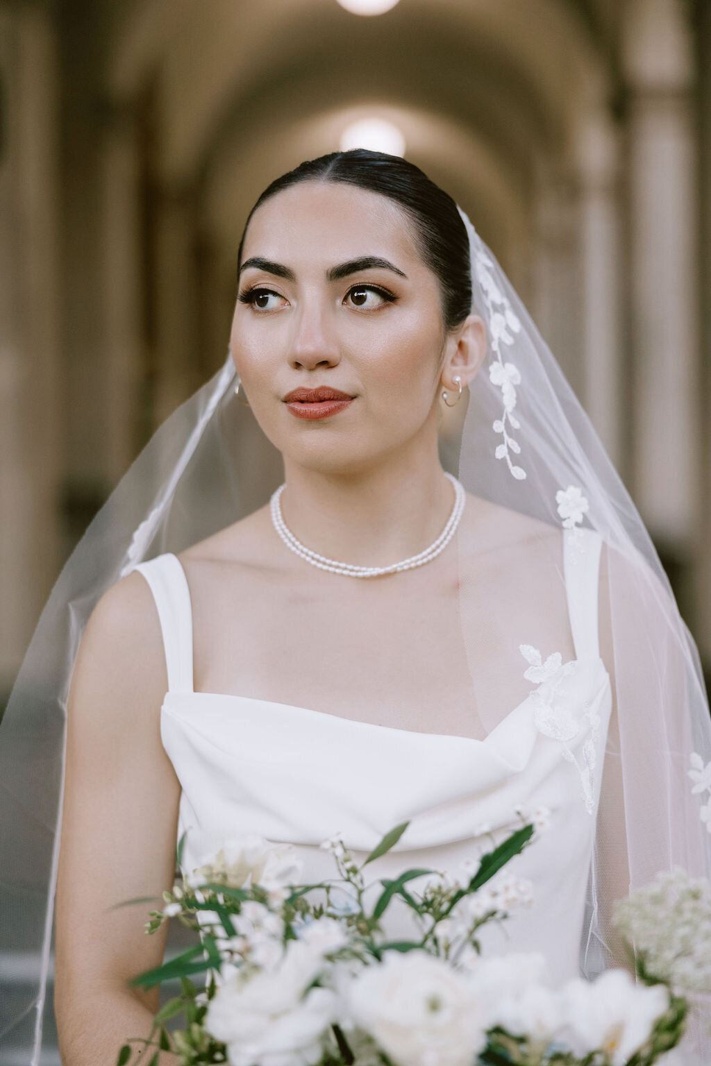 bridal portrait with glowing skin, spaghetti strap white crepe dress and florals wearing a veil