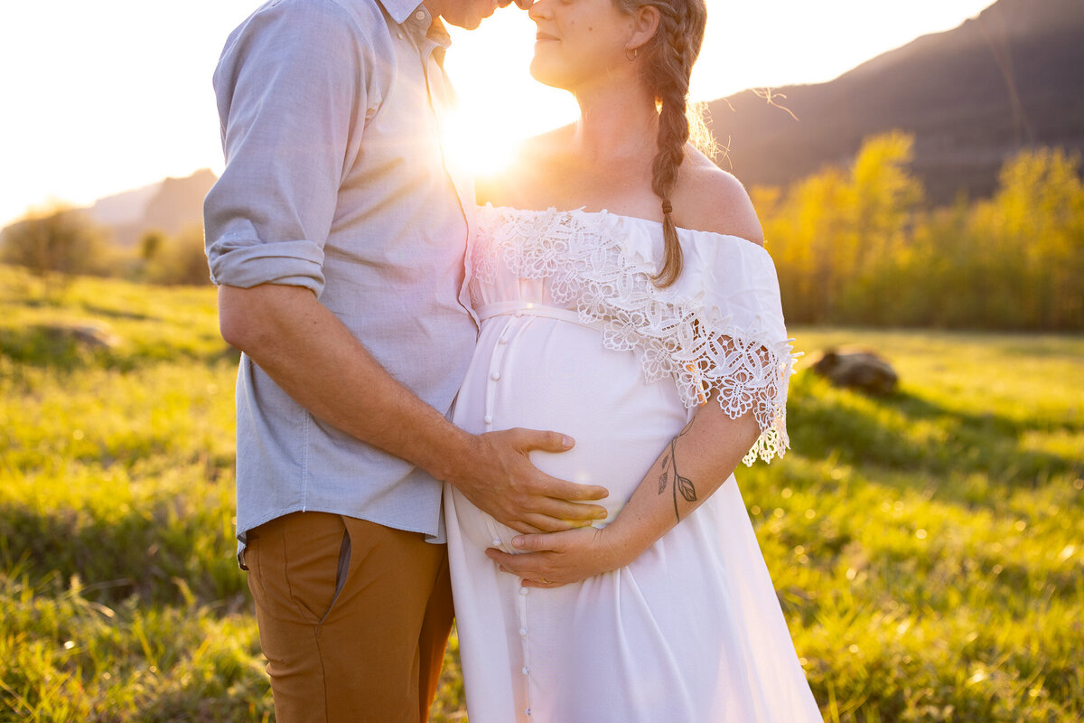 Pregnant couple embracing at sunset in field with Portland maternity photographer