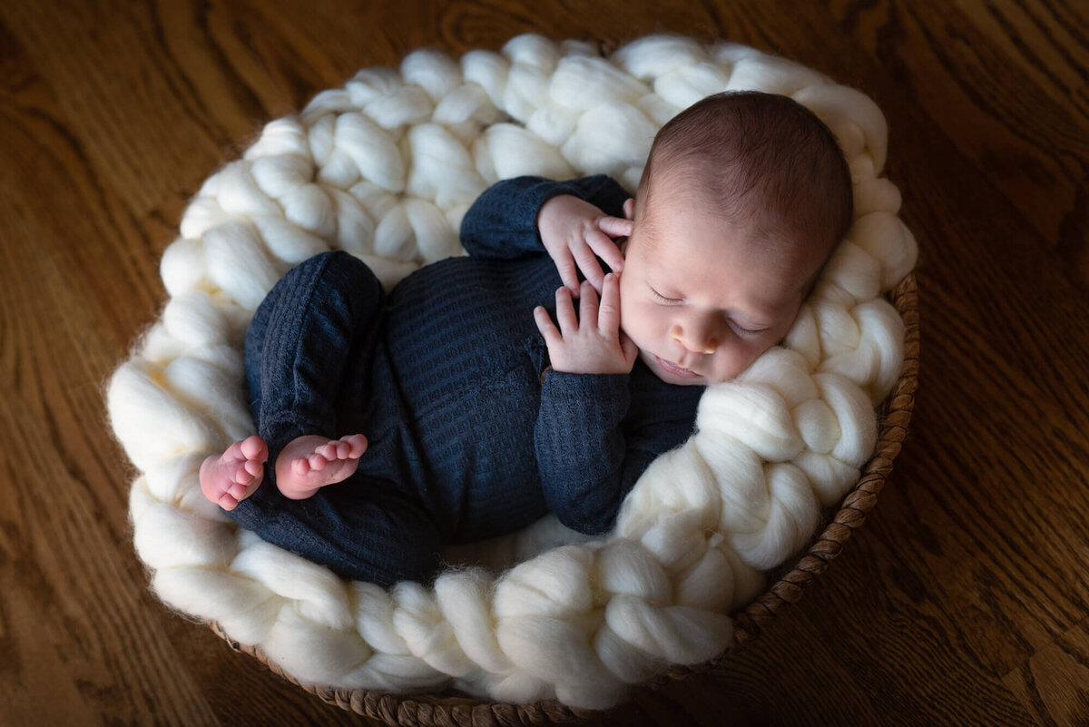 A newborn baby sleeping in a woven basket while wearing a blue onesie