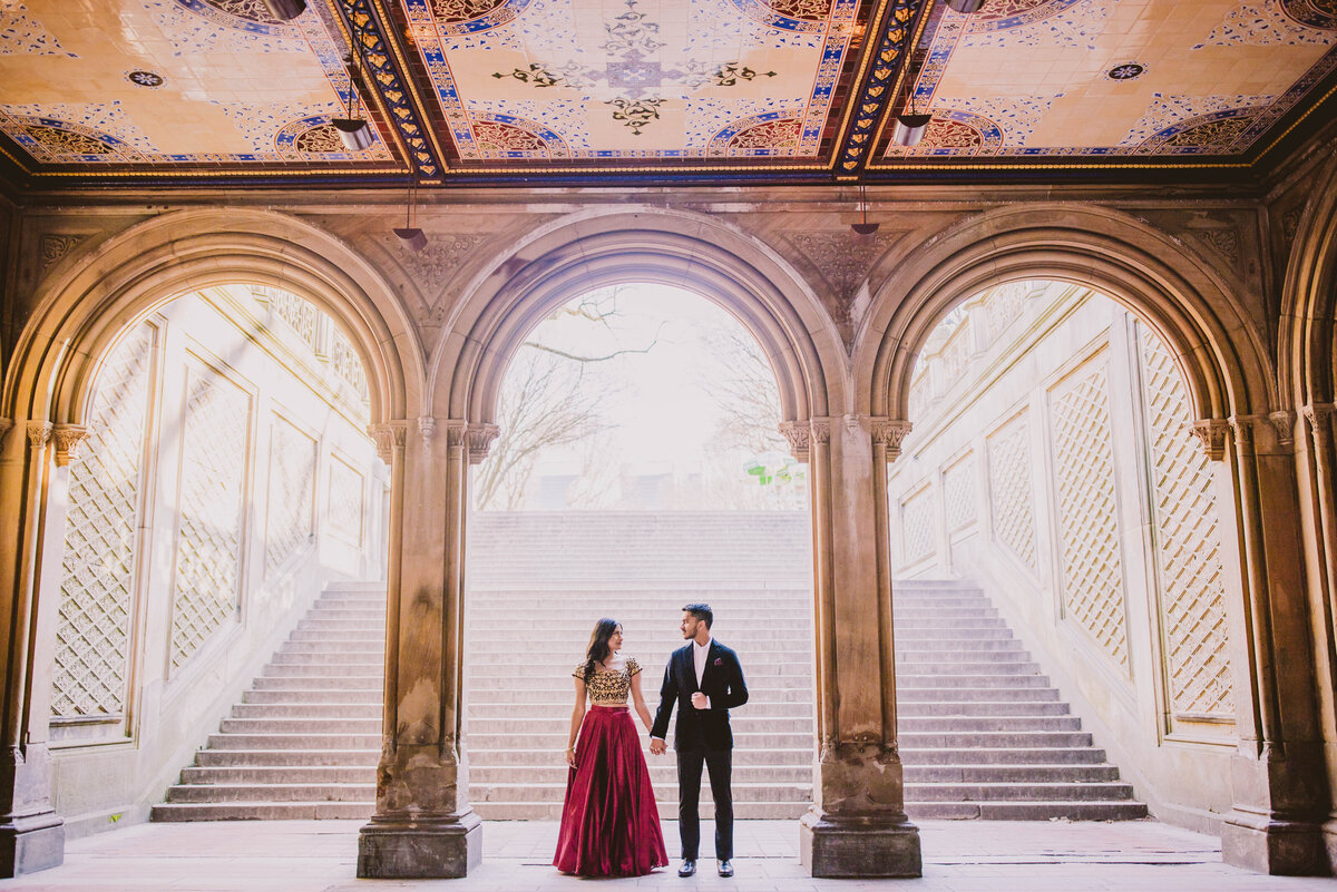 A couple wearing indian outfits standing under the 3 arches at central park at bethesda terrace
