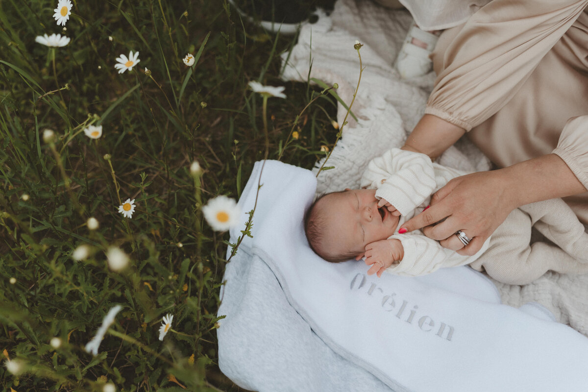Baby ligt op dekentje in een bloemenveld.