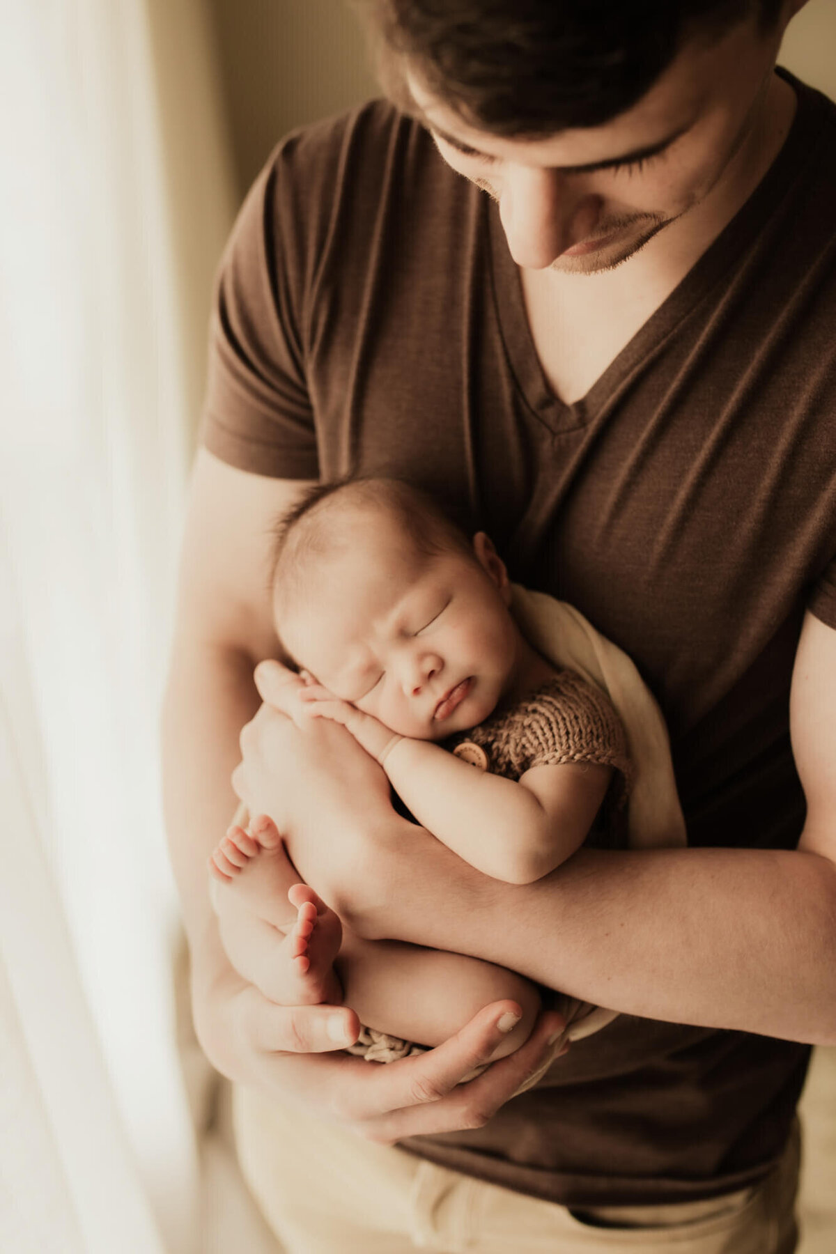 Father holds his newborn son in his arms as his baby sleeps.