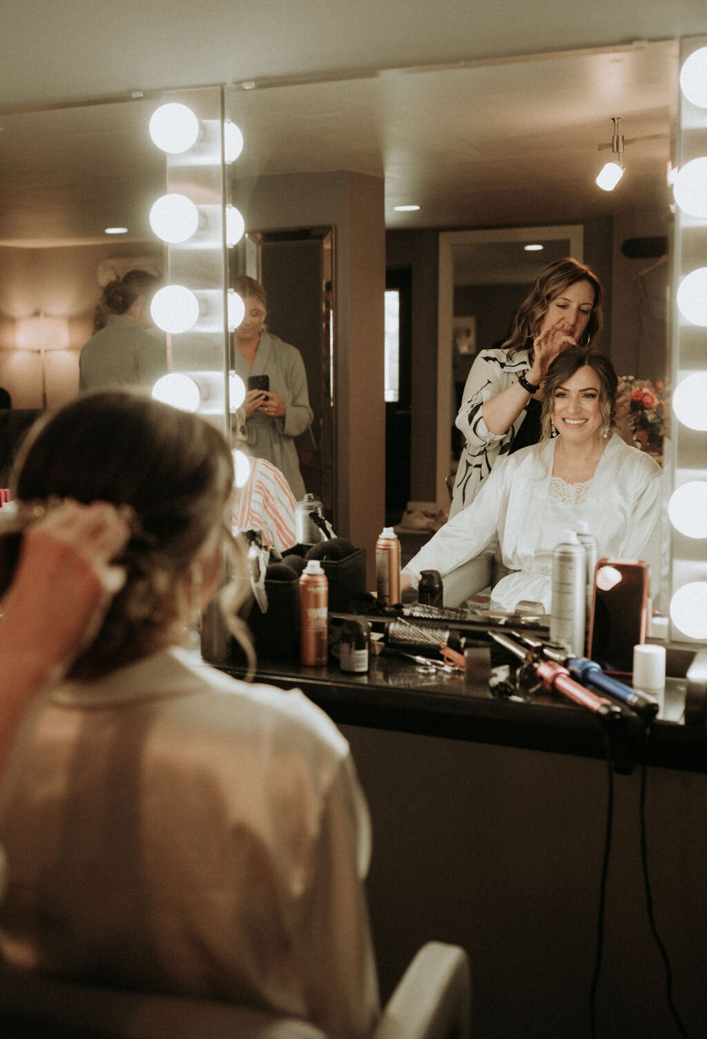 Bride sitting in the Willowbrook wedding preparation suite in front of the lighted make-up mirrors having her hair professionally styled