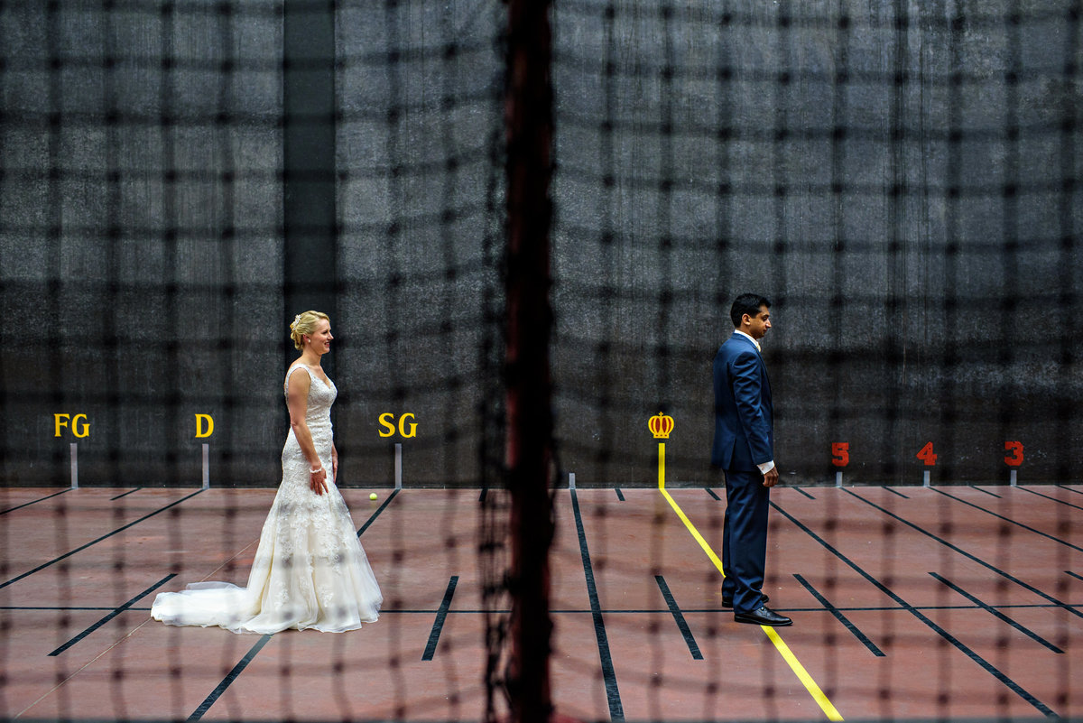A bride and groom have their first look on an inside tennis court before their wedding.