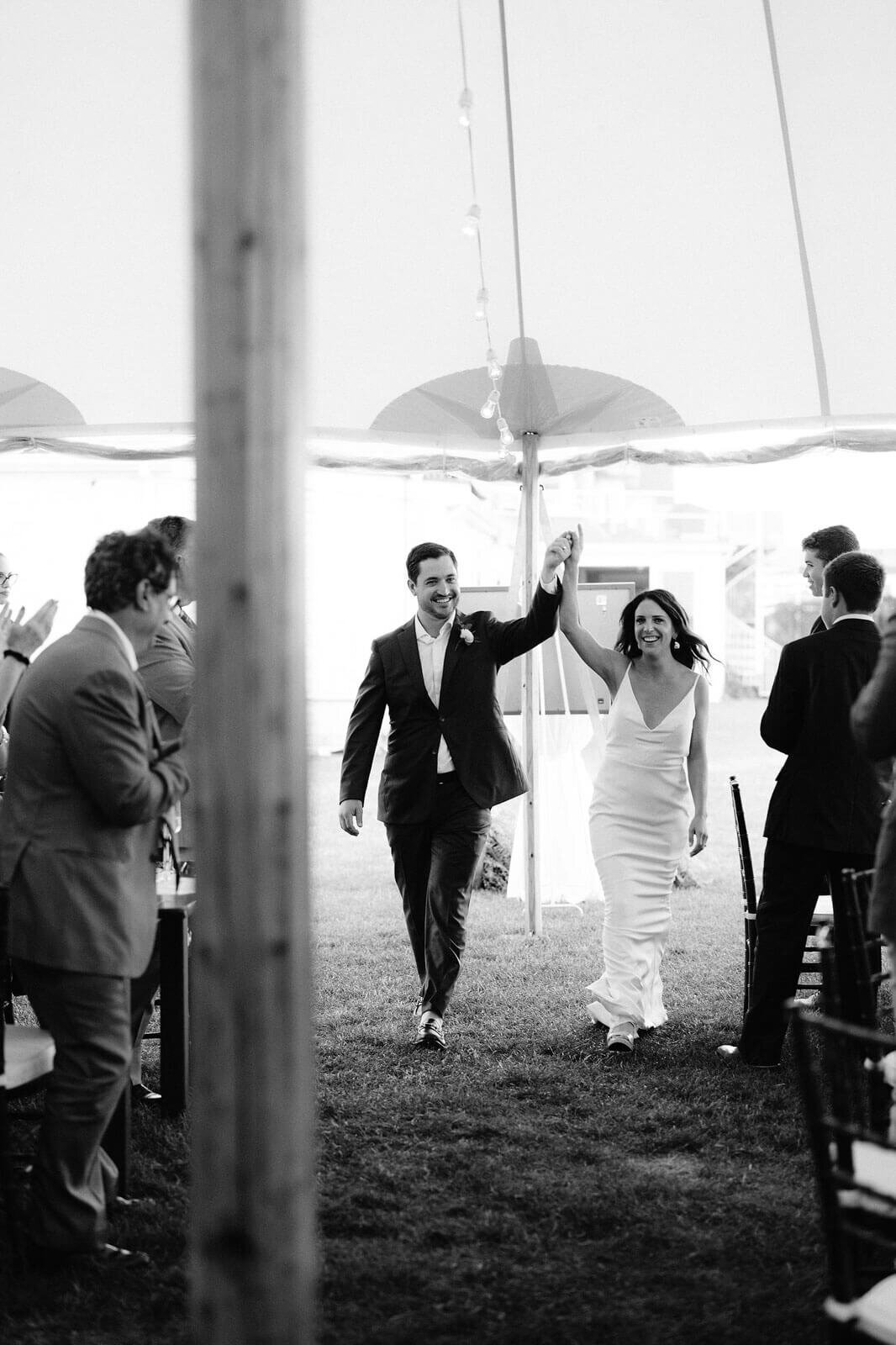 Black and white photo of the bride and groom entering the reception venue as the guests clapped, in Cape Cod Summer Tent, MA.