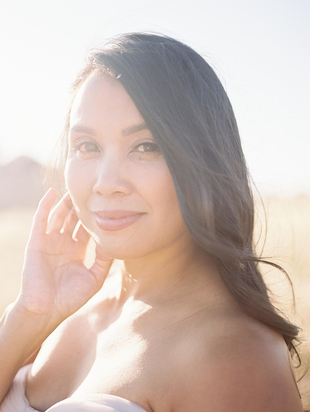 Close up of maternity photoshoot in San Francisco with a pregnant woman standing in a field against hills.