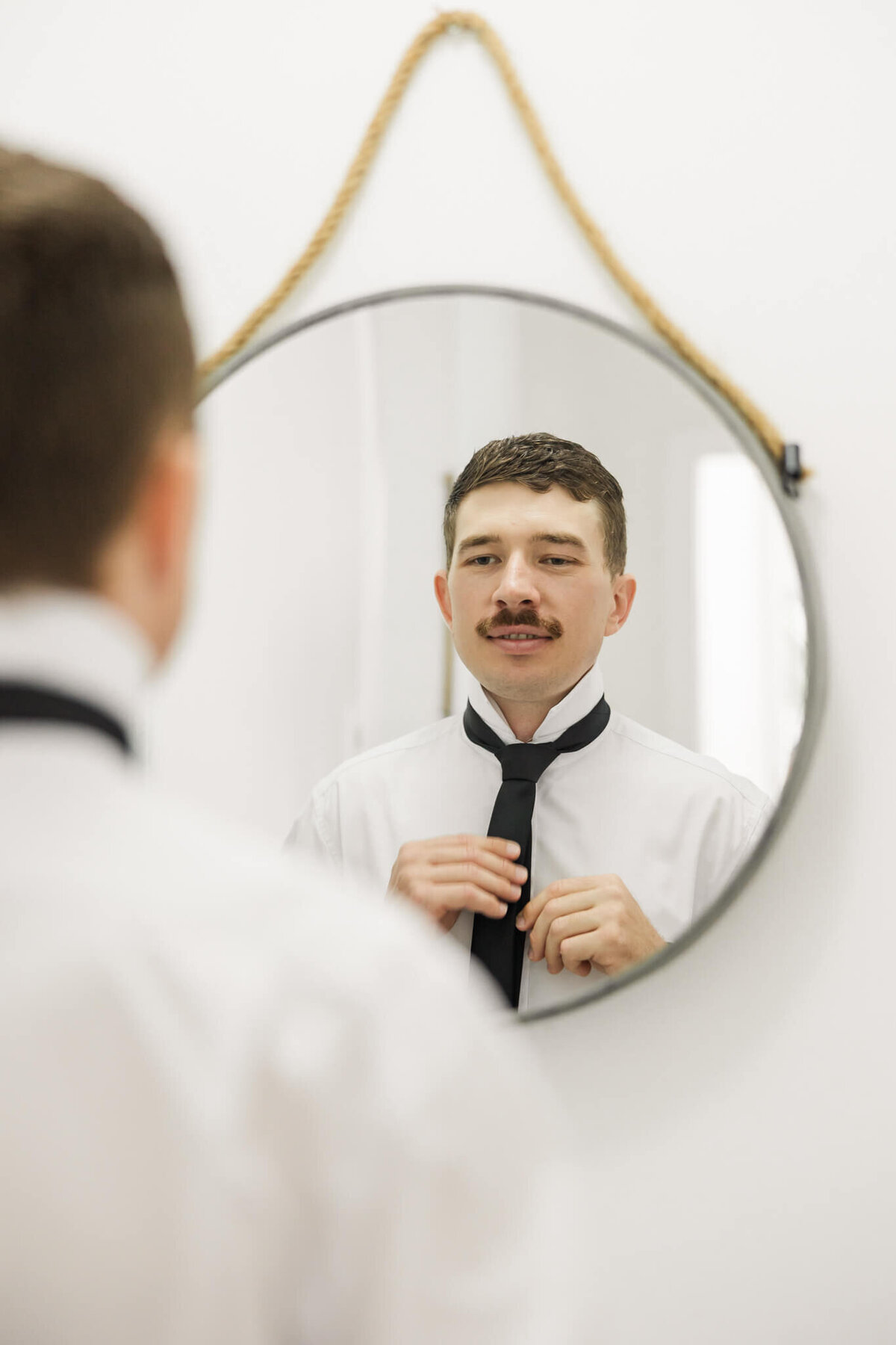 Groom adjust tie as he looks into a mirror before the wedding.