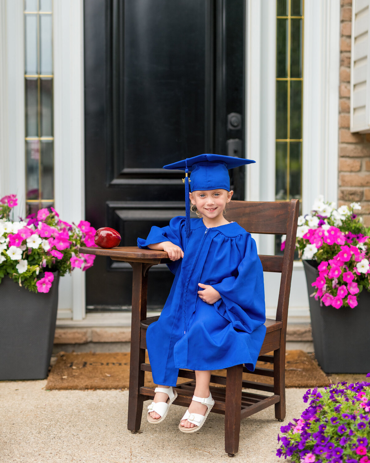 Child grad milestone photo with apple and wooden chair—celebrating a new chapter with a timeless smile.