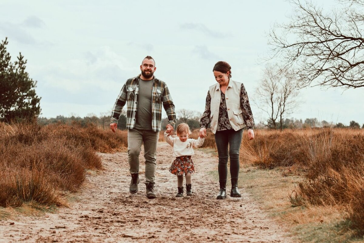 Familie foto buiten. Ouders en kind wandelen in de natuur. Jong gezin hand in hand op een pad.