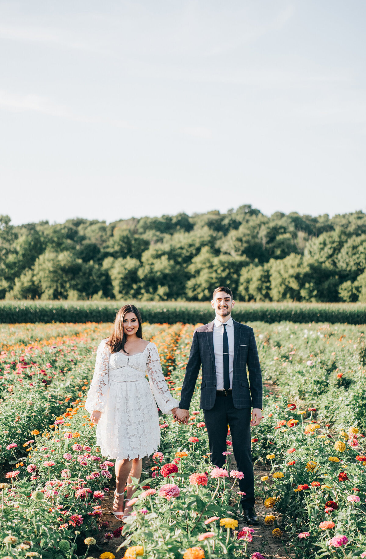Couple holding hands and walking through a whimsical wildflower field during their Summer engagement session