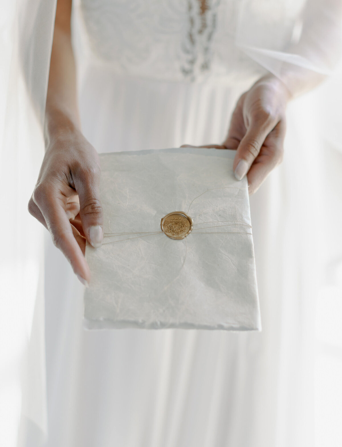 bride holds handmade paper wedding invitation, simple, ornate gold wax seal, Italy film wedding photographer