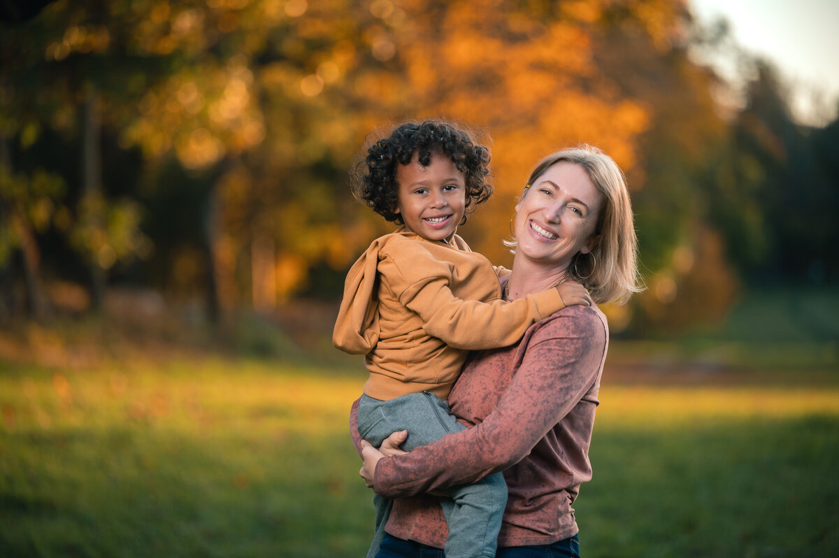 Mom holding son smiling with fall foliage in background