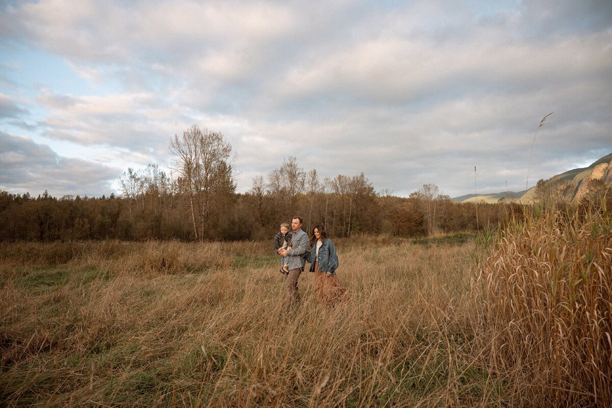 family of three walking outdoors in field at golden hour