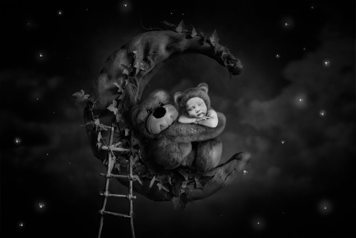 Black and white newborn photo of baby sleeping with a teddy bear on the moon