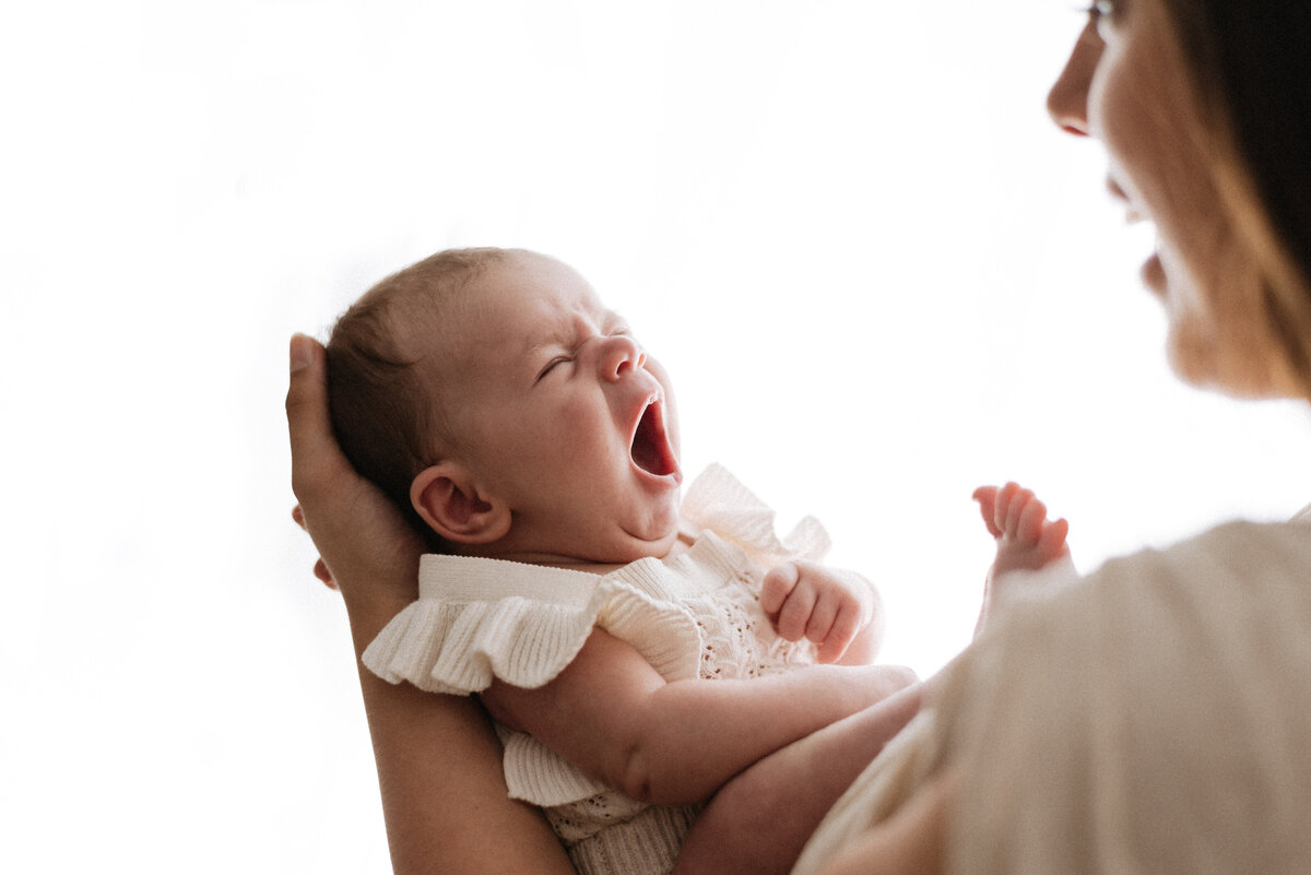 a mother holding her baby daughter who is yawning on newborn photoshoot in billingshurst